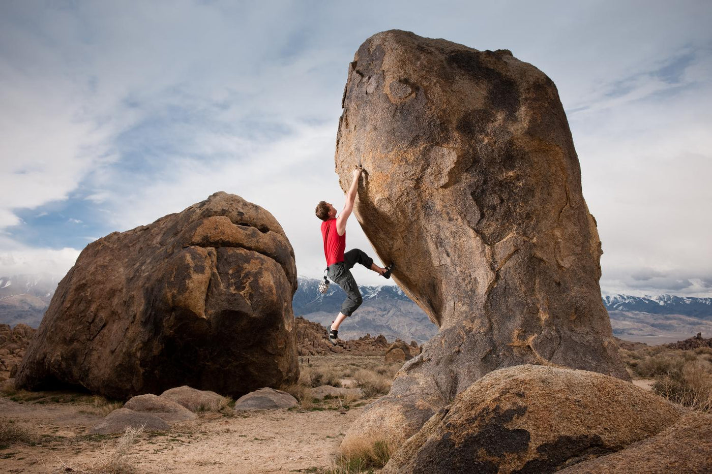 Man in a red shirt Bouldering up a tall boulder 