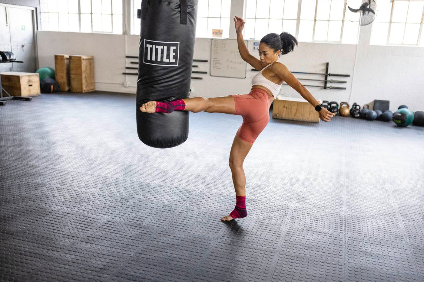 woman training for martial arts. She is kicking a punching bag while wearing a compression ankle brace