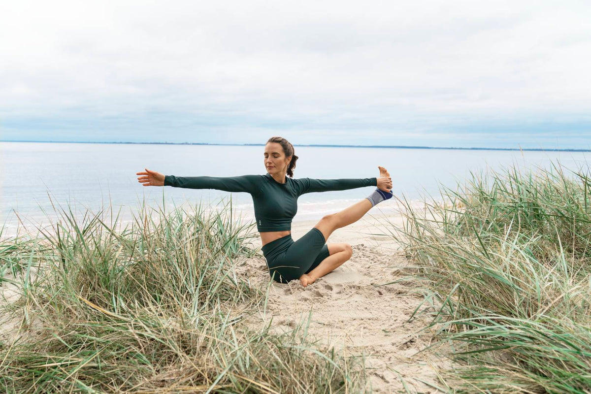 Woman doing a yoga pose on the beach while wearing an ankle brace to help support her ankle joint