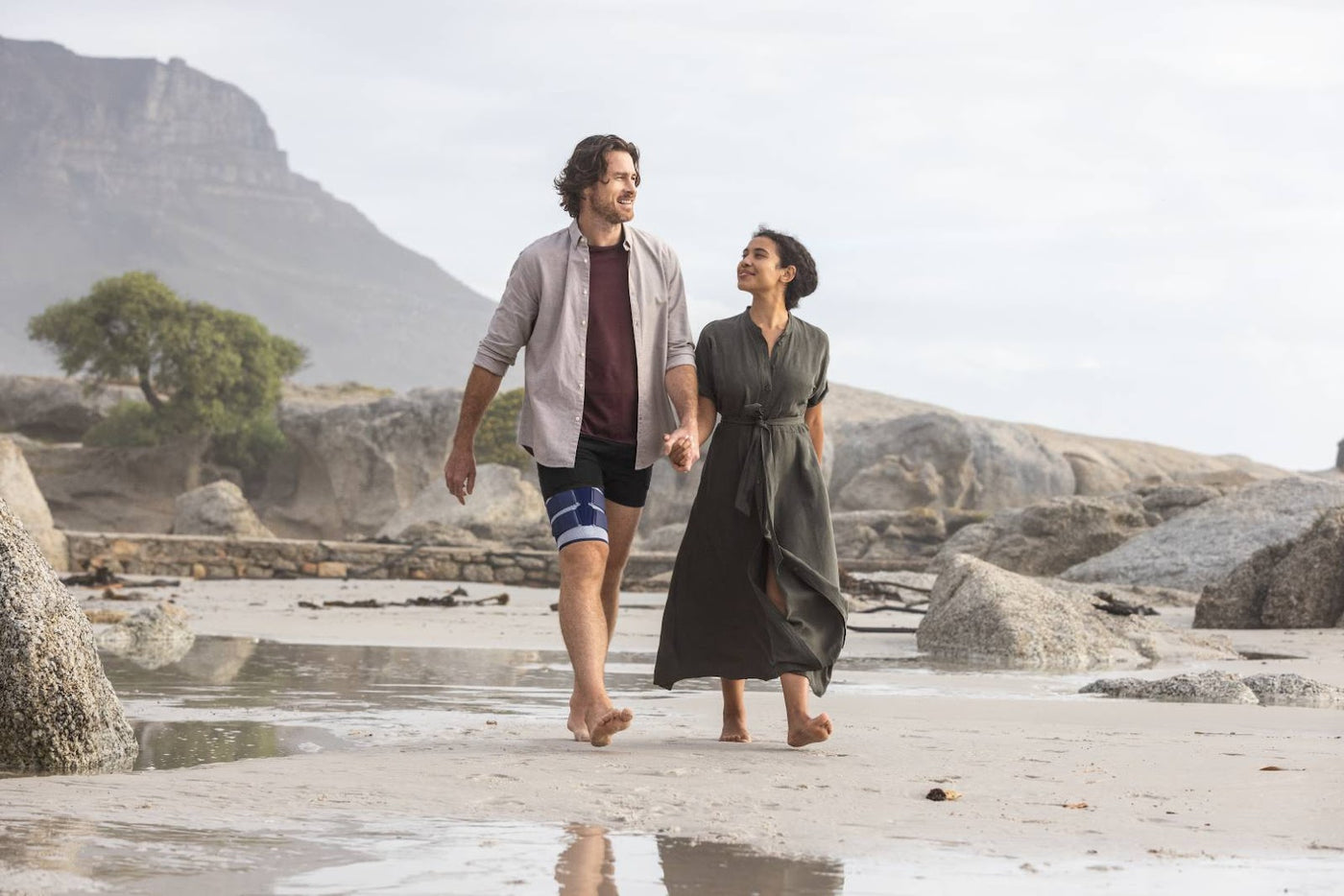 Man walking with his partner on the beach. He is wearing the MyoTrain Thigh Brace to manage thigh muscle pain