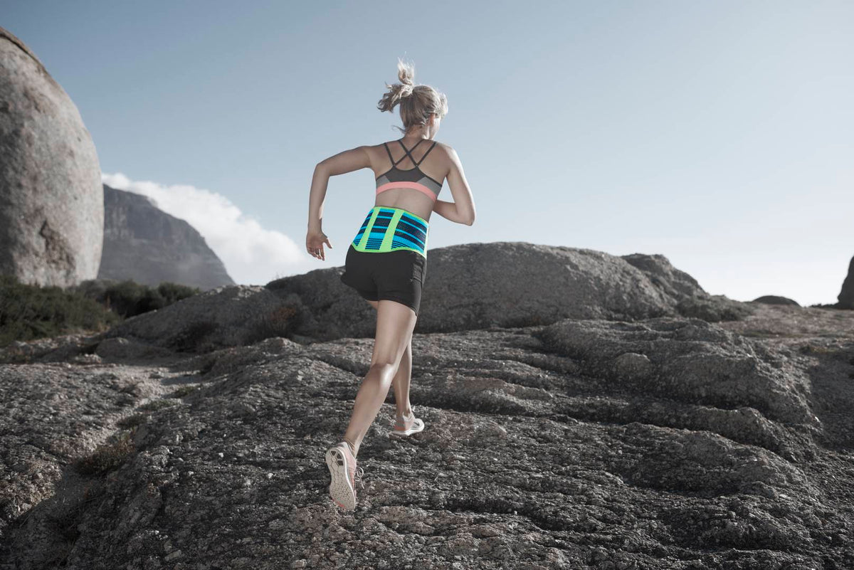 woman running up a rocky slope while wearing Bauerfeind's Sports Back Support