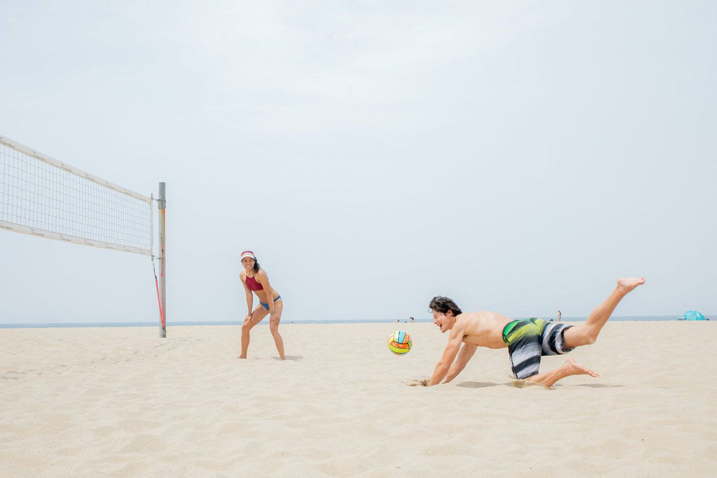 Young people playing beach volleyball. One of the players is falling in an attempt to catch the ball