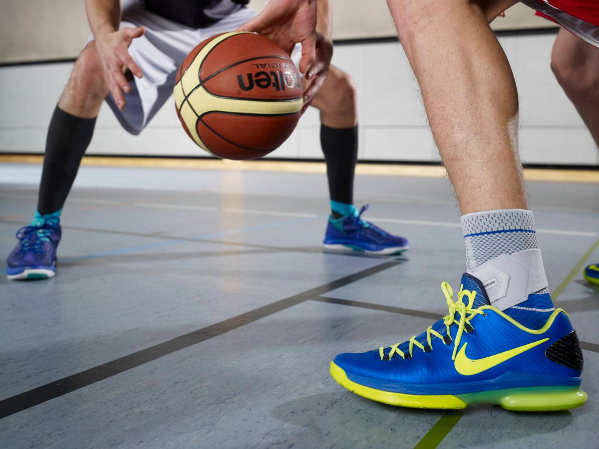 Image of two men playing basketball, one man is wearing a Bauerfeind ankle brace. Image relates to blog post with tips for selecting the right ankle brace for your injury