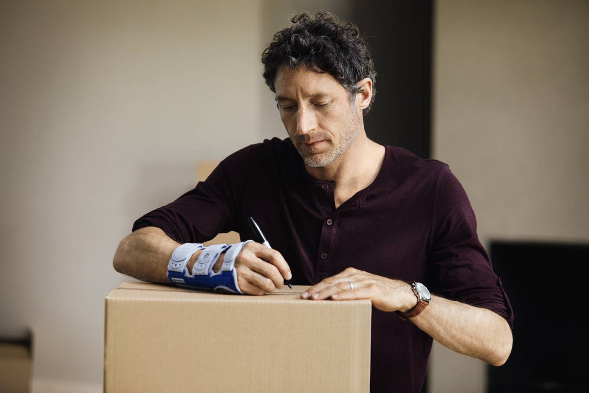 Man packing and writing on a box while wearing a ManuLoc wrist brace, a good way to support the wrist and stop it hurting