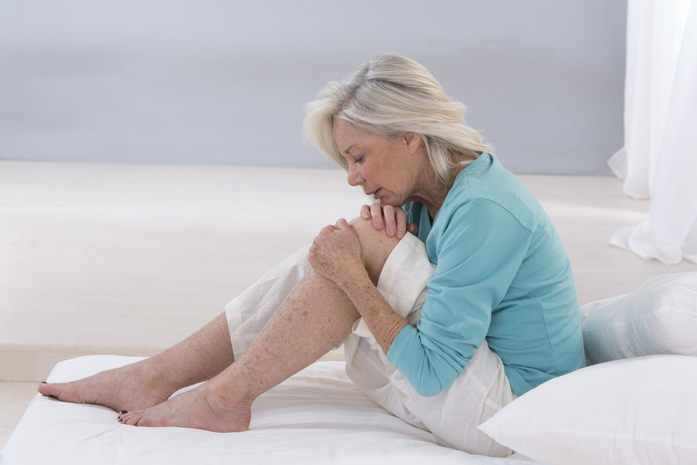 Knee Arthritis Treatment Without Surgery. Image of woman sitting on the floor holding one knee as though it is in pain.