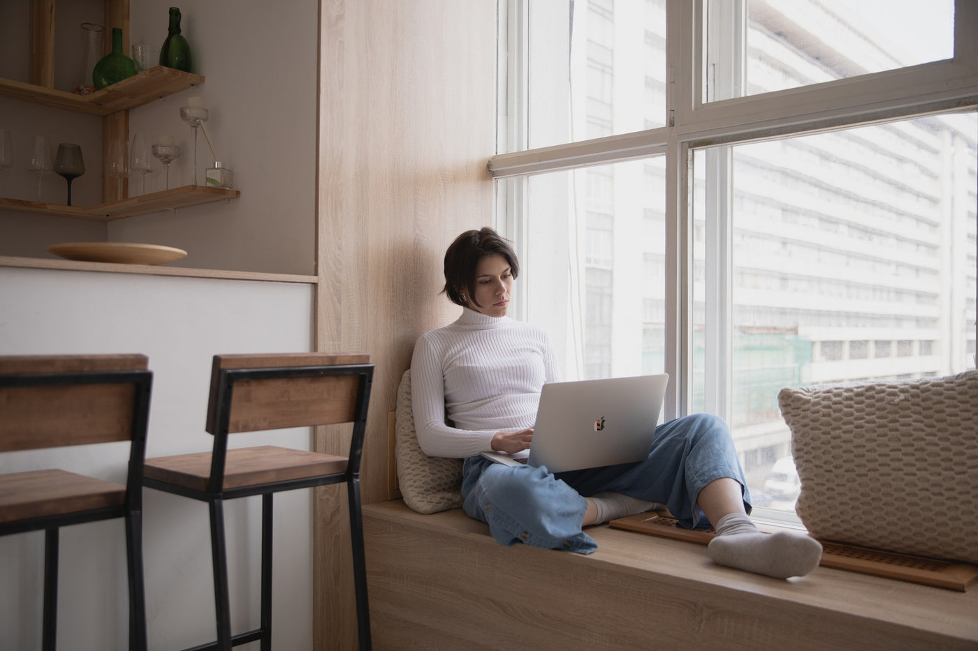 woman sitting on a window seat while working on her laptop, not an ideal set up for preventing back pain when working from home