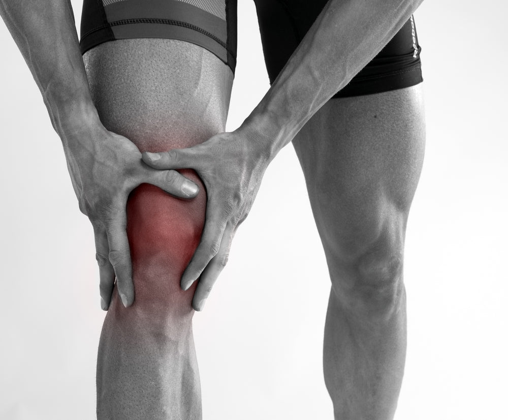 Black and white image of man holding his knee, the knee is highlight in red, indicating pain in the knee ligaments.
