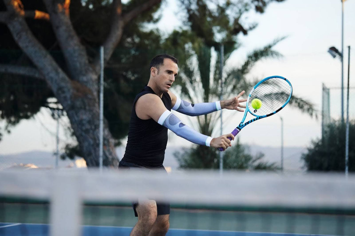 Man playing tennis. He is hitting backhand. He's wearing Bauerfeind's Sports Compression Arm Sleeves to reduce muscle fatigue while training