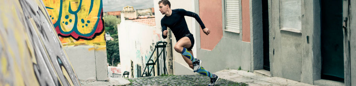 Wide shot of a triathlete in athletic gear and performance compression socks turning a corner as he's rinning down the street